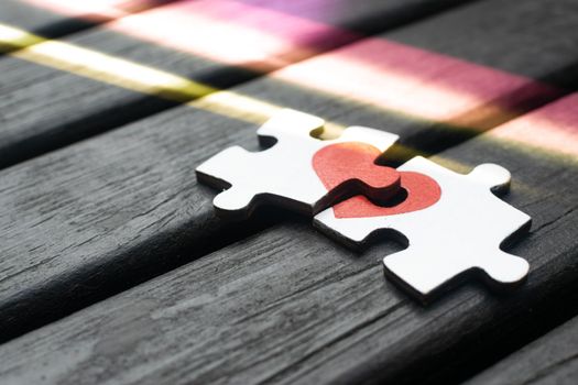Red heart is drawn on the pieces of the wooden puzzle lying next to each other on wooden background. Love concept.