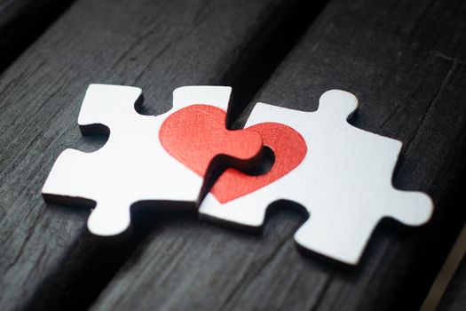 Red heart is drawn on the pieces of the wooden puzzle lying next to each other on wooden background. Love concept.