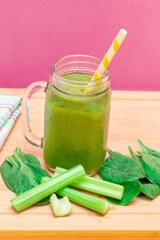 Fresh Green Smoothie of Apple, Celery, and Spinach in Glass Smoothie Jar with Yellow Cocktail Straw on Wooden Cutting Board. Vegan Detox Drink. Vegetarian Culture. Healthy Eating and Fruit Diet