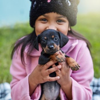 Cropped portrait of a cute little girl cuddling her puppy while sitting outside.