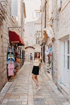 Girl tourist walking through ancient narrow street on a beautiful summer day in MEDITERRANEAN MEDIEVAL CITY , OLD TOWN bUDVA, MONTENEGRO. Young beautiful cheerful woman walking on old street at tropical town. Pretty girl looking at you and smiling