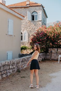 Girl tourist walking through ancient narrow street on a beautiful summer day in MEDITERRANEAN MEDIEVAL CITY , OLD TOWN bUDVA, MONTENEGRO. Young beautiful cheerful woman walking on old street at tropical town. Pretty girl looking at you and smiling