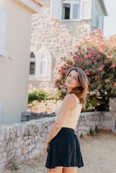 Girl tourist walking through ancient narrow street on a beautiful summer day in MEDITERRANEAN MEDIEVAL CITY , OLD TOWN bUDVA, MONTENEGRO. Young beautiful cheerful woman walking on old street at tropical town. Pretty girl looking at you and smiling