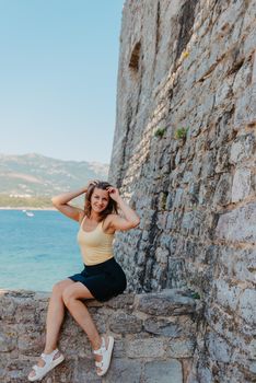 Beautiful girl sitting on a stone wall, in background is the blue sea, Budva, Montenegro