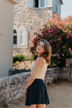 Girl tourist walking through ancient narrow street on a beautiful summer day in MEDITERRANEAN MEDIEVAL CITY , OLD TOWN bUDVA, MONTENEGRO. Young beautiful cheerful woman walking on old street at tropical town. Pretty girl looking at you and smiling