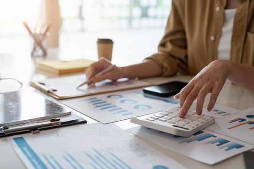 Close up of business woman or accountant working on calculator to calculate business data, accountancy document and laptop computer at office, business concept.