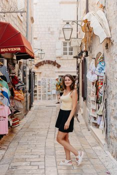 Girl tourist walking through ancient narrow street on a beautiful summer day in MEDITERRANEAN MEDIEVAL CITY , OLD TOWN bUDVA, MONTENEGRO. Young beautiful cheerful woman walking on old street at tropical town. Pretty girl looking at you and smiling