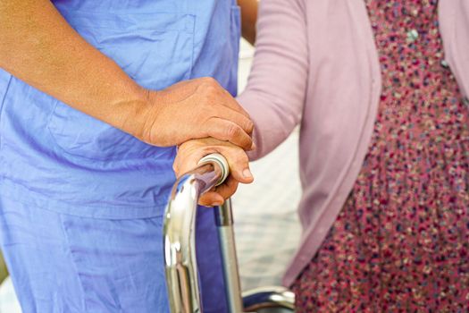 Caregiver help Asian elderly woman disability patient walk with walker in nursing hospital, medical concept. 