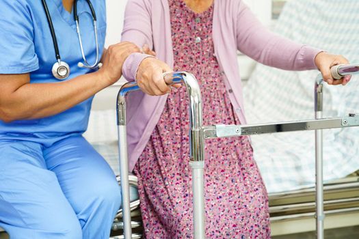 Caregiver help Asian elderly woman disability patient walk with walker in nursing hospital, medical concept.    