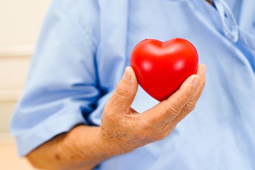 Asian elder senior woman patient holding red heart in hospital.  