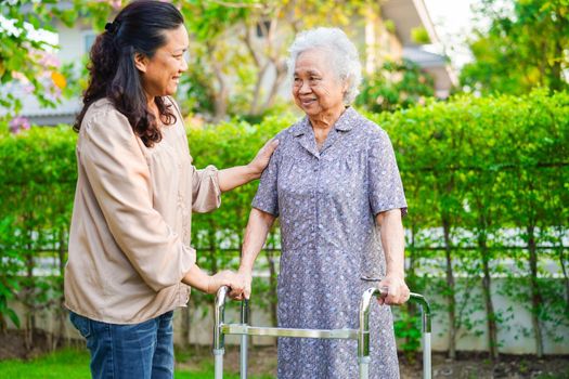 Caregiver help Asian elderly woman disability patient walk with walker in park, medical concept.