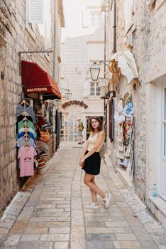 Girl tourist walking through ancient narrow street on a beautiful summer day in MEDITERRANEAN MEDIEVAL CITY , OLD TOWN bUDVA, MONTENEGRO. Young beautiful cheerful woman walking on old street at tropical town. Pretty girl looking at you and smiling