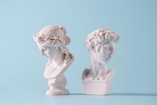 Two small antique style Roman or Grecian busts of young men facing away from each other on blue