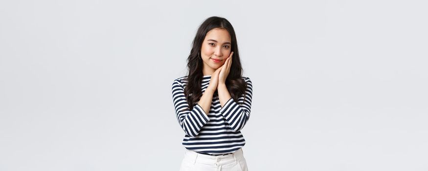 Lifestyle, people emotions and casual concept. Tender asian woman with beautiful face, touching cheek gently and gazing camera, advertising beauty product, cosmetics or skincare items.