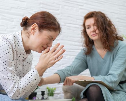 Caucasian woman crying at psychotherapy session. The female doctor calms the patient and holds her hand