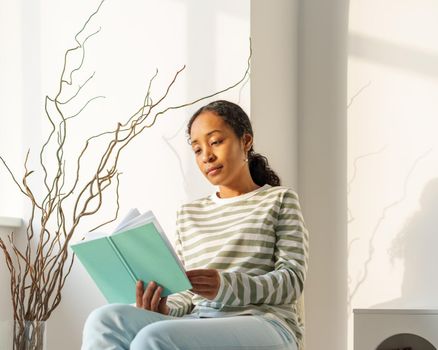 African-American woman looking at book. Leisure activity in spare time. Slow paced lifestyle. Concept of modern young bookworm. Focusing on literature. Finding inspiration while reading