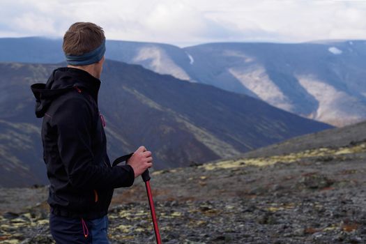 a young man with trekking poles in a bandana stands against the backdrop of mountains. photo