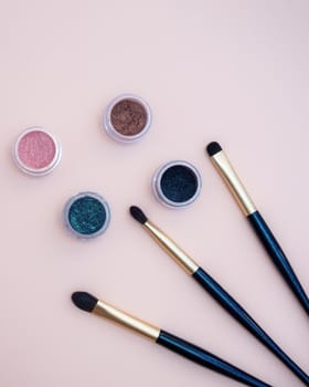 Composition with decorative makeup products golden brushes and colorful eye shadows on pastel pink background. photo