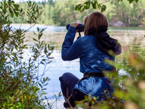 Young woman looking through binoculars at birds on the lake. Birdwatching, zoology, ecology. Research in nature, observation of animals Ornithology autumn bird migration selective focus, soft focus. photo