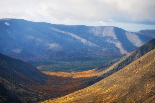Autumn colorful tundra on the background mountain peaks in cloudy weather. Mountain landscape in Kola Peninsula, Arctic, Khibiny Mountains.