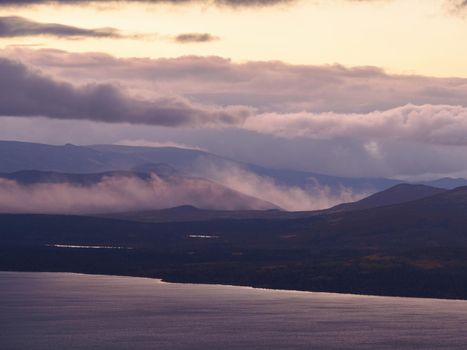 A beautiful mountain landscape with a lake in the distance and low creeping clouds. Autumn mountains of Khibiny in Russia. photo