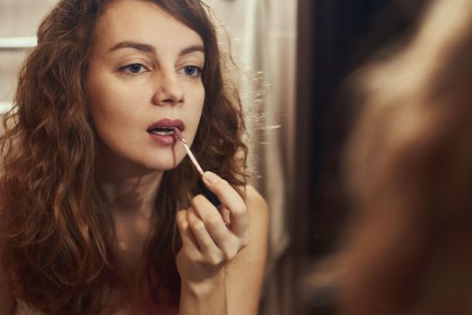 Woman paint her lips with lipstick in front of mirror,