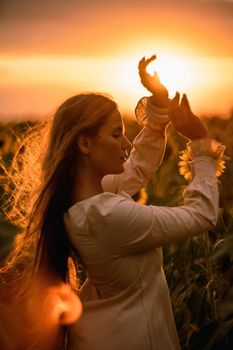 Beautiful middle aged woman looks good in a hat enjoying nature in a field of sunflowers at sunset. Summer. Attractive brunette with long healthy hair