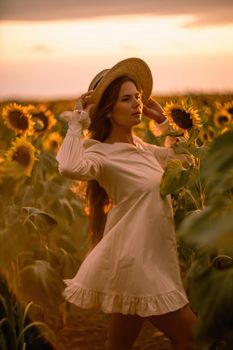 Beautiful middle aged woman looks good in a hat enjoying nature in a field of sunflowers at sunset. Summer. Attractive brunette with long healthy hair