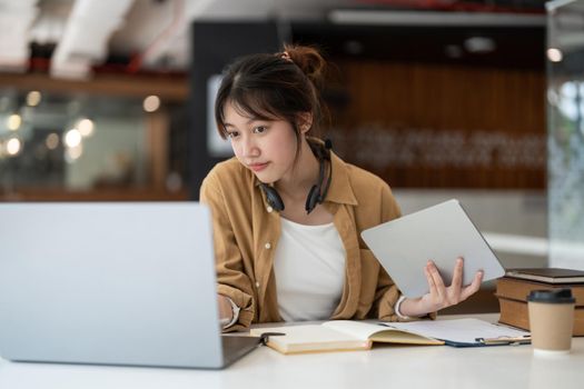 Smiling Asian young female using headset looking at laptop screen listen and learning online courses. Happy business woman with headphones video call for customer service.