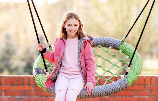 Beautiful little girl swinging on a round swing at the playground