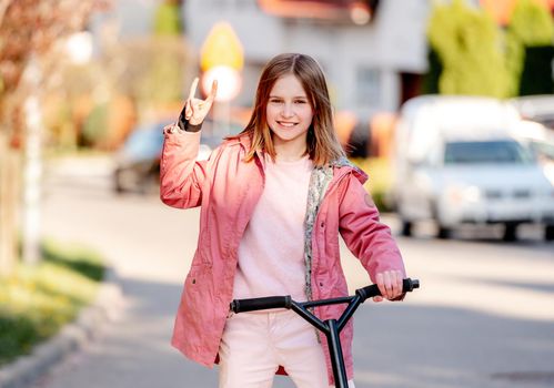 Funny little girl rides a kick scooter on a street near home