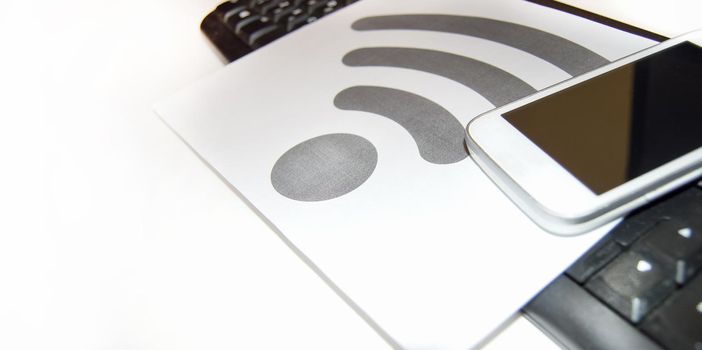 Wi-Fi symbol on a piece of paper near the computer keyboard and mobile phone, wireless Internet, copy space.