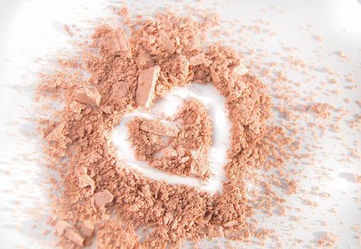 Scattered crumbs of face powder or eye shadow in the shape of a heart on a white background, makeup concept.