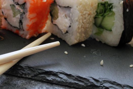 Rolls with shrimp, crab stick, cheese, cucumber, vegetables and sushi sticks on a black board. Close-up. Japanese cuisine.