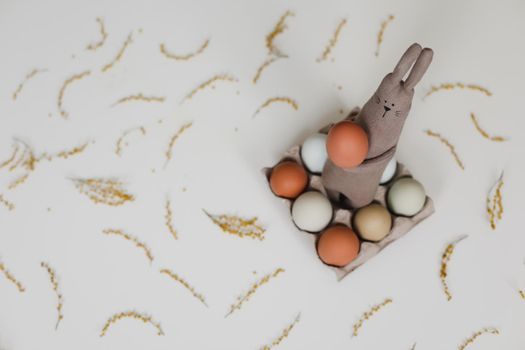 Funny handmade bunny rabbit toy with colorful chicken eggs and yellow mimosa flowers. Easter gift concept.