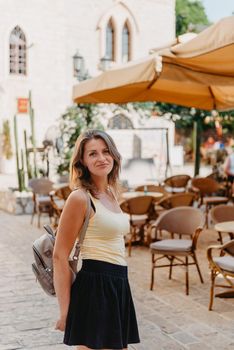 Girl tourist walking through ancient narrow street on a beautiful summer day in MEDITERRANEAN MEDIEVAL CITY , OLD TOWN bUDVA, MONTENEGRO. Young beautiful cheerful woman walking on old street at tropical town. Pretty girl looking at you and smiling