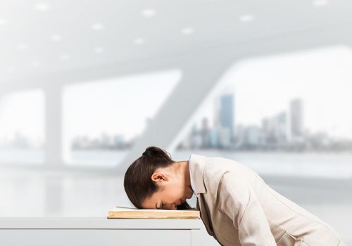 Exhausted business woman face down sleeping on desk with notebook. Tired corporate employee relaxing in office. Young female worker in white suit overworking. Accounting and paperwork deadline