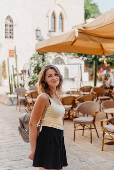 Girl tourist walking through ancient narrow street on a beautiful summer day in MEDITERRANEAN MEDIEVAL CITY , OLD TOWN bUDVA, MONTENEGRO. Young beautiful cheerful woman walking on old street at tropical town. Pretty girl looking at you and smiling