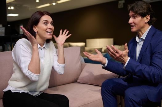 Charming elegant European dark-haired woman and handsome Caucasian mature man in business suit having a fun talk, sitting together in a pink comfortable velour sofa