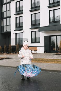 Toddler girl with colorful umbrella outdoors at rainy day.