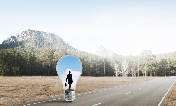 Young businesswoman trapped inside of light bulb on asphalt road