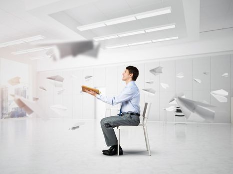 young businessman with book on office chair