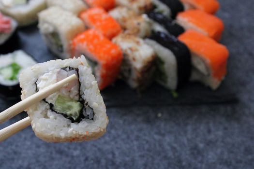 Rolls with shrimp, sesame, tuna, bacon, cheese, cucumber, vegetables and sushi sticks on a black board. Close-up. Japanese cuisine. Background.