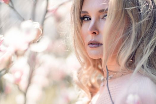 Portrait of a beautiful happy middle aged woman enjoying the smell in a blooming spring garden. Beautiful magnolia bushes, large flowers