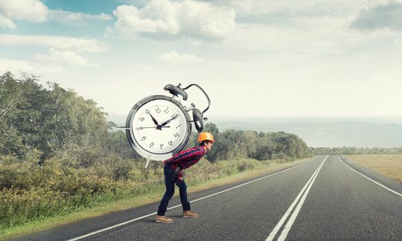 Builder man in helmet carrying alarm clock on back