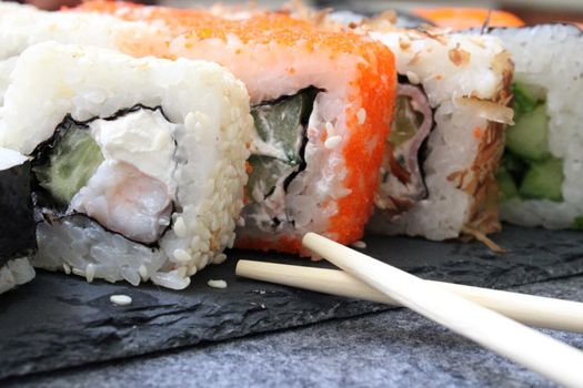 Rolls with shrimp, sesame, tuna, bacon, cheese, cucumber, vegetables and sushi sticks on a black board. Close-up. Japanese cuisine. Background.