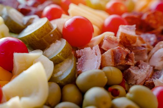 cherry tomatoes, sweet peppers, pickled cucumbers, pickled garlic, olives, sausage, different cheese, bacon on wooden plate. Snack food