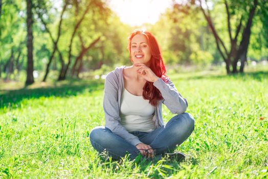 Portrait of a young attractive woman. Sitting cross-legged in the park