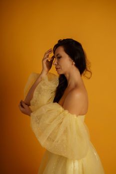 Profile portrait of a beautiful middle-aged woman in a yellow dress, her hair pulled up against a yellow background.