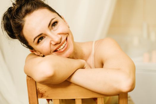 Portrait of a middle-aged woman, smiling with her arms folded in front of her face, her hair pulled up. The brunette is in a good mood. On a light background